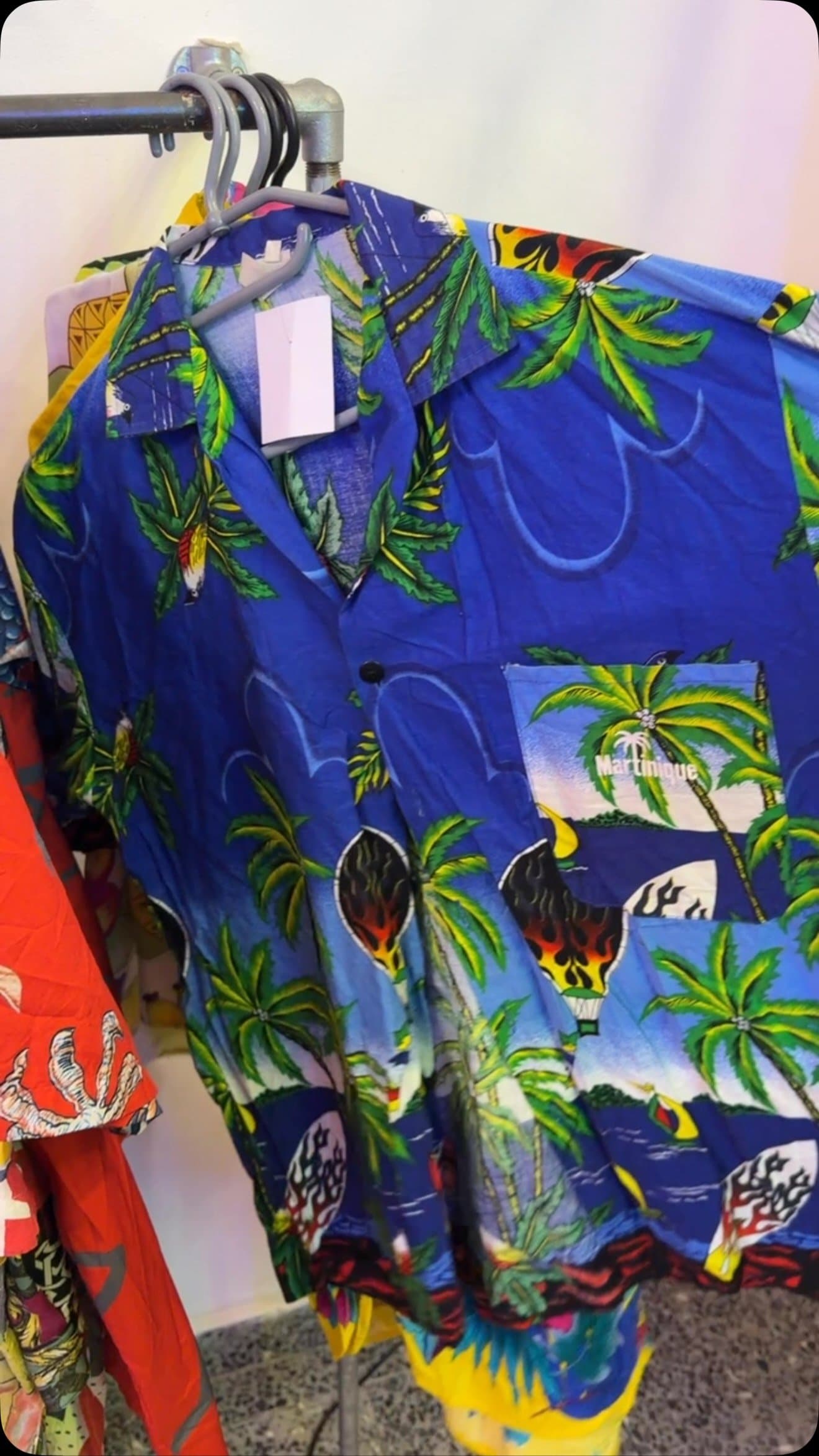 Koszula hawajska z palmami na wieszaku w sklepie vintage